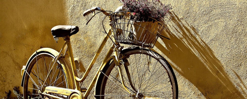 Imagem cortada de uma bicicleta com cesto frontal com flores encostada em uma parede rústica