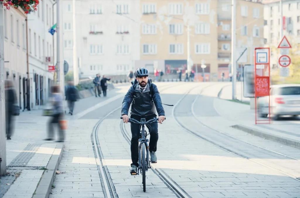 Homem usando capacete e roupas escuras pedalando na rua