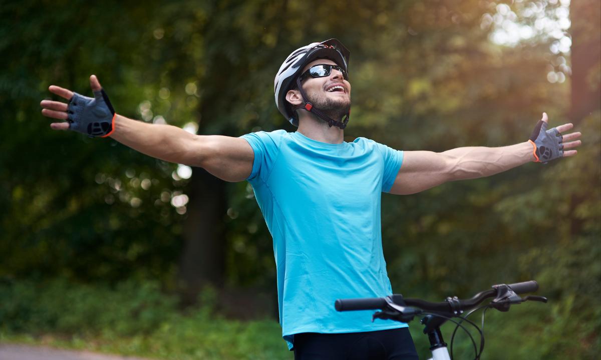 homem de braços abetos em sua bike, ao ar livre, com expressão d satisfação e felicidade