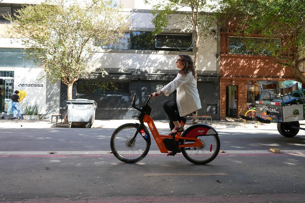 Mulher andando com a bike da Tembici por bairro de São Paulo.