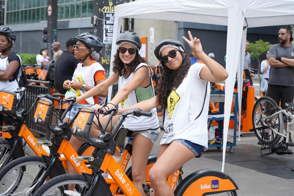 garotas acenando para foto, usando as bikes da tembici e equipamentos de segurança para realizar seu passeio 