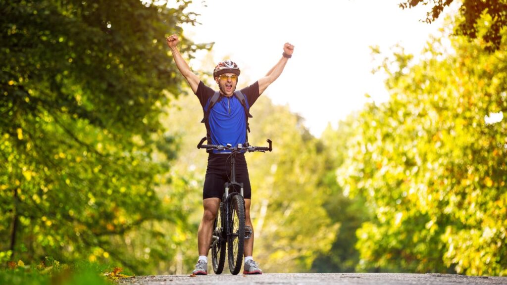 ciclista comemorando com os braços para o alto, em meio a uma bela paisagem verde