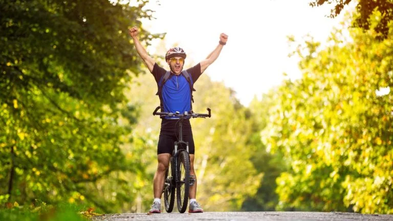 ciclista comemorando com os braços para o alto, em meio a uma bela paisagem verde