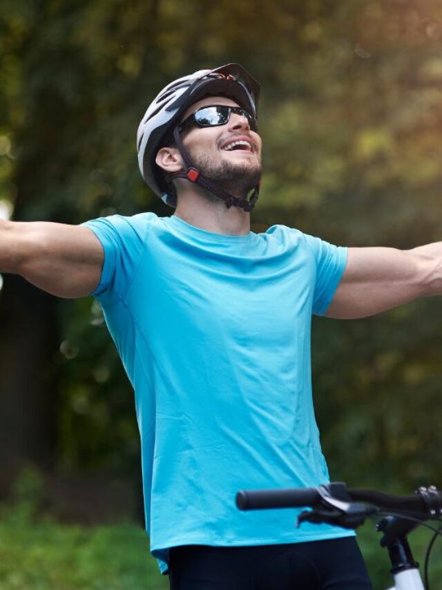 homem de braços abetos em sua bike, ao ar livre, com expressão d satisfação e felicidade