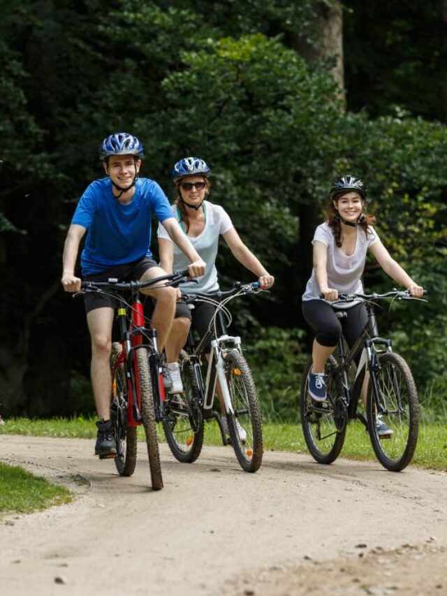 três pessoas praticando a atividade de pedalar de bicicleta em um parque