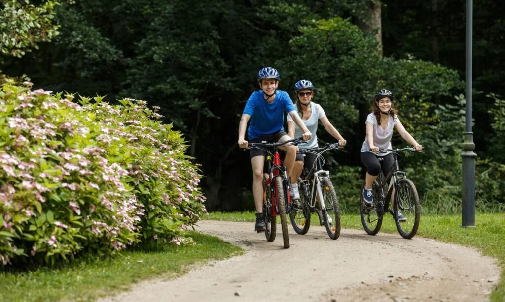 três pessoas praticando a atividade de pedalar de bicicleta em um parque