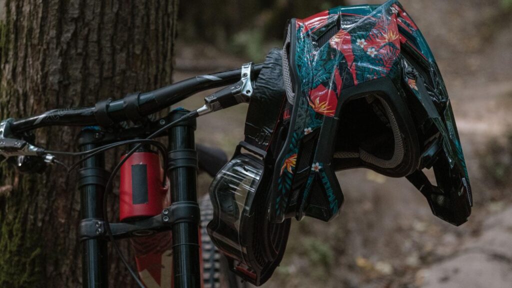 capacete full race encaixado no guidão de uma bike, que esta encostada em uma árvore.