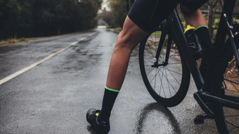 homem se preparando para pedalar na chuva, em uma estrada