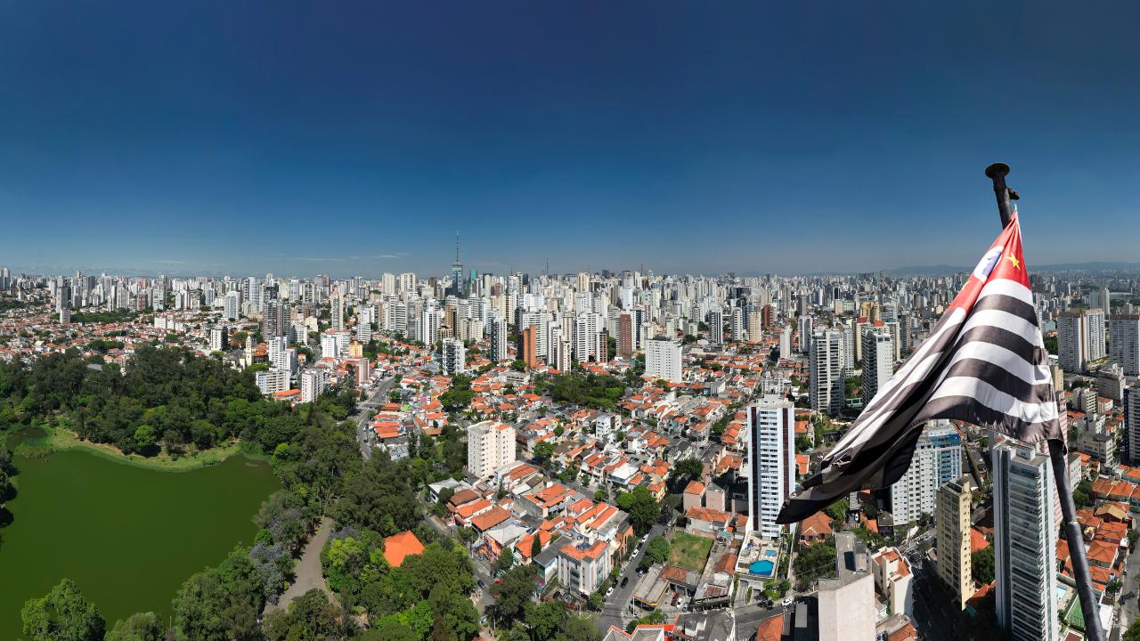 imagem aerea da cidade de São Paulo, uma bandeira do ESTADO a direita e um parque a esqueda da imagem.