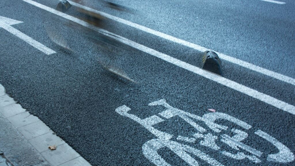 Imagem de uma ciclofaixa, e um vulto de um ciclista passando por ela.