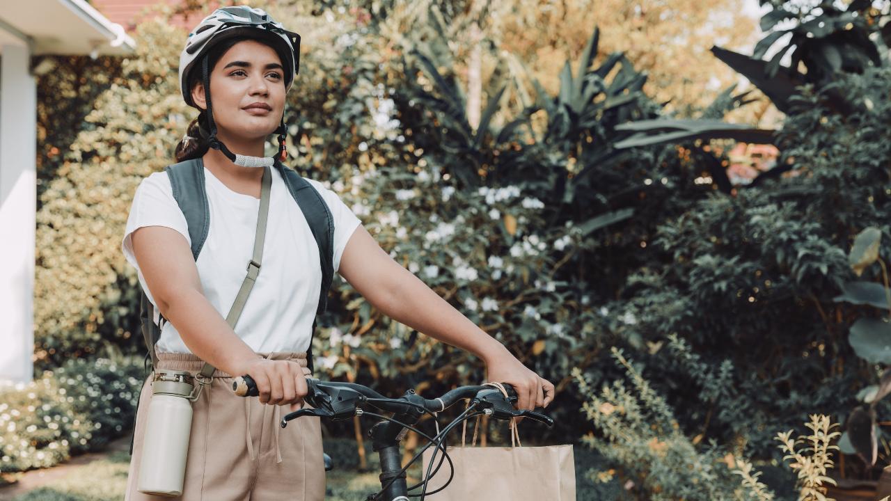 mulher com capacete de proteção, mochila e garrafa de água, indo trabalhar de bicicleta